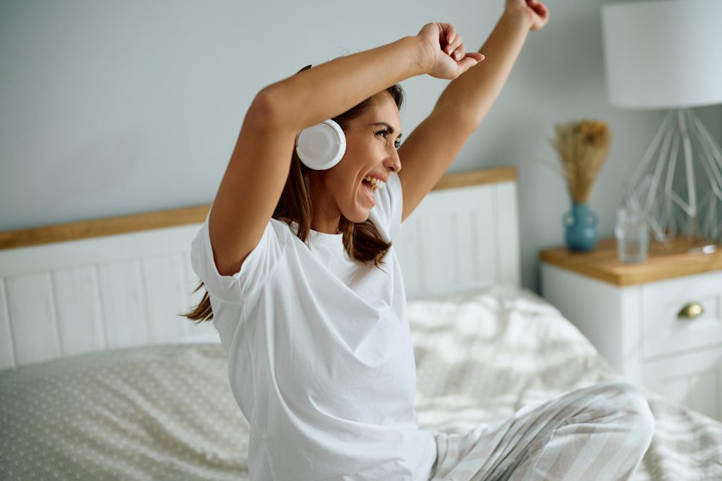 Mujer despreocupada escuchando música y cantando en el dormitorio